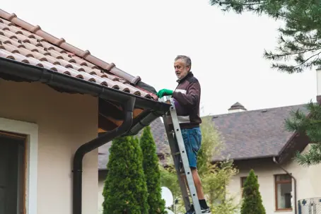 man on ladder inspecting home gutters